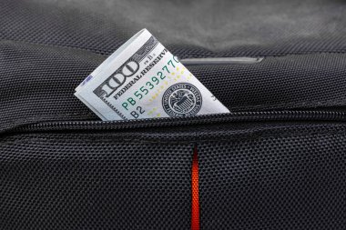 A hundred dollar bill peeks out of a backpack pocket. Tourist scam. Losing money while traveling. Lure for a thief. High quality photo