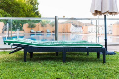 Önde iki boş yeşil ve beyaz güneş uzanmış çimenli zeminde bir havuzda.