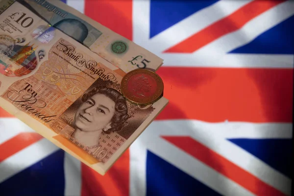 Two British five and ten pound bills and one pound coin on the flag of the United Kingdom.