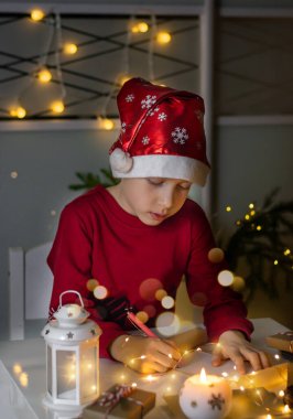 Dikey fotoğrafçı çocuk kırmızı Noel şapkalı Noel Baba 'ya mektup yazıyor..