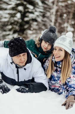 Portrait of happy family in winter forest looking at camera and smiling, vertical photo.