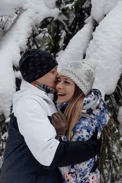 Man and woman in love hugging and kiss on in the forest. Snowy winter background. Vertical photo.
