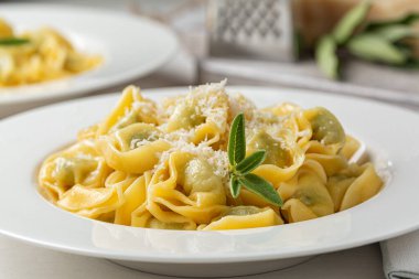 Ispanak ve ricotta ile doldurulmuş tortelloni yakın plan, erimiş tereyağı ve adaçayı yapraklarıyla kızartılmış. Parmesan peyniri rendelenmiş. 