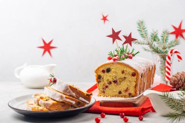 Beyaz masa ve arka planda taze yaban mersini ve biberiyeyle süslenmiş yaban mersinli, kuru üzümlü ve bademli Noel meyveli pasta. Arka planda yıldızlar olan bir Noel süsü. Kapatın. Seçici odak.