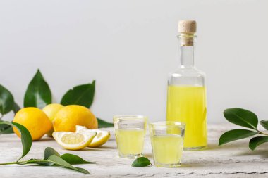 Küçük bardakta limoncello ve şişe - İtalyan limon likörü, taze İtalyan limonları. Işık arkaplanı, kopyalama alanı.