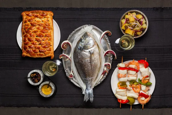 Festive fish and seafood dinner concept. Baked dorado fish, fish pie, potato salad, seafood skewers.  Feast tradition. Top view.