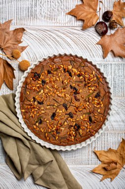 Autumn castagnaccio cake. Plain chestnut flour vegan cake,  made with water, olive oil, pine nuts, rosemary and raisins. Italian, Tuscany  rural dessert on white wood table.