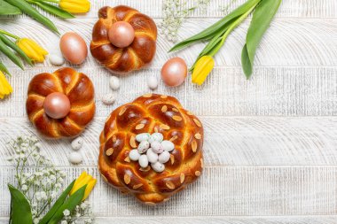 Paskalya arkaplanı İtalyan tarzı örgü ekmek ve pembe metalik yumurta, şeker. Ev yapımı hamur işi. Sarı laleler. Beyaz ahşap arka plan. Üst görünüm, alanı kopyala.