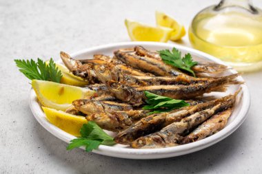 Tavada kızartılmış ançüezi limon ve maydanozla birlikte beyaz tabağa koy. Beyaz arkaplan.