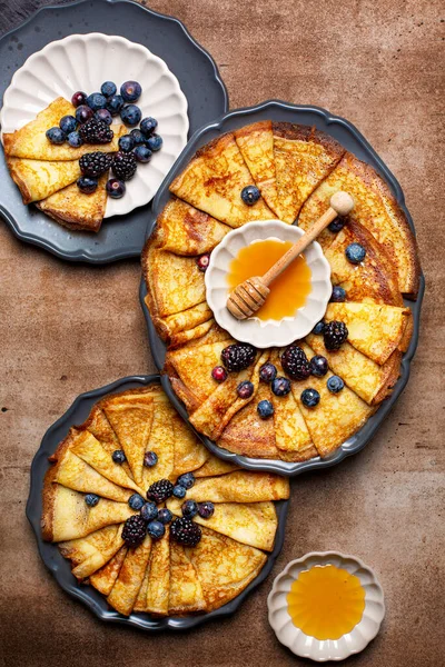 Ballı krep, yabanmersini ve böğürtlen. Üst manzara, koyu kaslı arka plan. Kahvaltıda ya da çay saatinde ev yapımı ince krep ya da krep. Dikey resim.