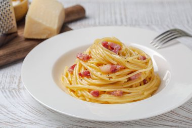 Beyaz tabakta spagetti carbonara. Makarna, pancetta ve yumurta sarısı, parmesan peyniri ve karabiberden yapılmış sos. Arka planda sert peynir.