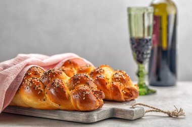 Pembe kapaklı iki somun ev yapımı Challah ekmeği ve arka planda bir bardak şarap. Açık gri arkaplan. Seçici odaklanma. Boşluğu kopyala.
