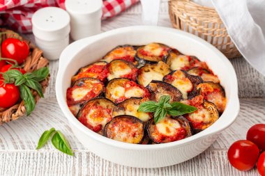 İtalyan yemeği ev yapımı fırında patlıcan di melanzane, mozzarella, domates ve fesleğen yapraklarından yapılır. Beyaz ahşap bir masada.