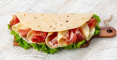 Tahta kesim tahtasında piadina romagnola, prosciutto crudo di Parma ile geleneksel İtalyan düz ekmeği - İtalyan kuru jambonu, mozzarella peyniri, marul. 