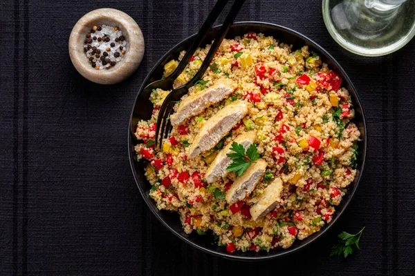 Couscous salad. Chicken breast and vegetables, tomatoes, avocado, bell pepper, parsley and lemon juice. Black table surface. Directly above.