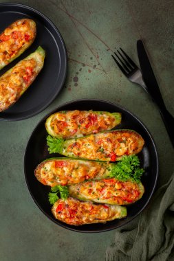 Dinner with oven baked Zucchini stuffed with chicken meat, belle peppers, tomatoes and cheese on a dark green table surface. Directly Above, vertical image.