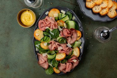 Meat and vegetable salad with roast beef, parmesan cheese, garlic toast bread, spinach and cucumber. Mustard. Table top view.
