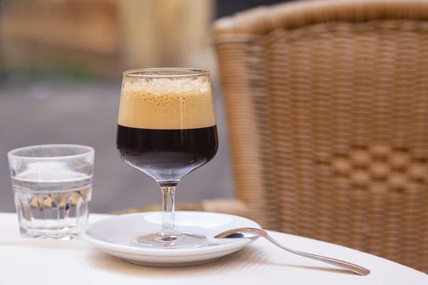 Caffe shakerato in a tall glass, in an outdoor italian cafe. Cold shaked coffee with a foam made in a shaker with ice. 