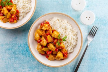 Kırmızı biber ve ananasla pişirilmiş hindi körili tabaklar. Basmati pilavı. Mavi bir masa yüzeyinde iki porsiyon.