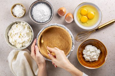 Cheesecake pişirmek, kadın elleri ezilmiş kurabiye ve tereyağından kek kabuğu yapmak. Ana malzemeler: yumuşak, taze krem peynir, yumurta, şeker tozu, ekşi krema, mısır nişastası. Üst görünüm.