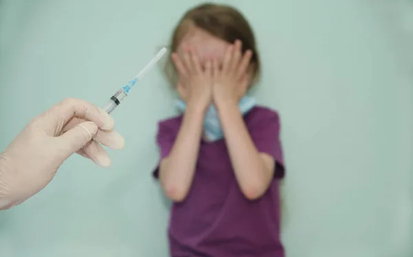 Çocuk, aşıya karşı bir işaret olarak elleriyle yüzünü kapadı.