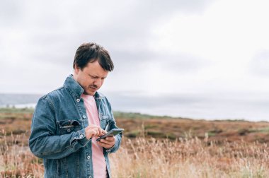 İrlanda denizinde uçurumun kenarında duran ve akıllı telefondan fotoğraf çeken bir gezgin. İngiltere 'de, Anglesey' de, Güney Yığını Deniz Feneri 'nde harika bir manzara.