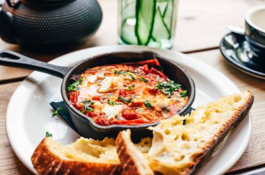 Baharatlı domates, kırmızı biber, feta, yumurta, kişniş ve ev yapımı ekşi hamur ile taze yapılmış shakshuka, demir tavada servis edilir, sağlıklı vejetaryen kahvaltısı.
