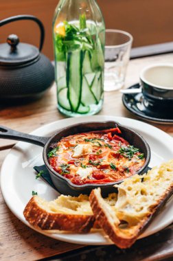 Baharatlı domates, kırmızı biber, feta, yumurta, kişniş ve ev yapımı ekşi hamur ile taze yapılmış shakshuka, demir tavada servis edilir, sağlıklı vejetaryen kahvaltısı.