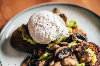 Haşlanmış yumurtadan sağlıklı bir kahvaltı, kırılmış avokado, ekşi ekmeğin üstünde ızgara mantar, seçici odaklanma, sığ DoF