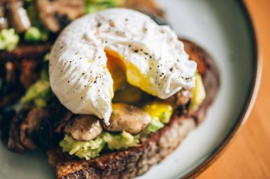 Haşlanmış yumurtadan sağlıklı bir kahvaltı, kırılmış avokado, ekşi ekmeğin üstünde ızgara mantar, seçici odaklanma, sığ DoF