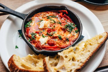 Baharatlı domates, kırmızı biber, feta, yumurta, kişniş ve ev yapımı ekşi hamur ile taze yapılmış shakshuka, demir tavada servis edilir, sağlıklı vejetaryen kahvaltısı.