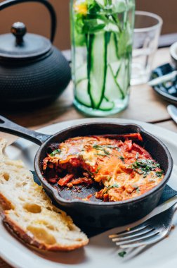 Yarısı yenmiş taze Shakshuka ile baharatlı domates, kırmızı biber, feta, yumurta, kişniş ve ev yapımı ekşi ekmek, demir tavada servis edilir, sağlıklı vejetaryen kahvaltısı.