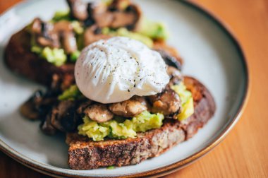 Haşlanmış yumurtadan sağlıklı bir kahvaltı, kırılmış avokado, ekşi ekmeğin üstünde ızgara mantar, seçici odaklanma, sığ DoF