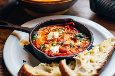 Baharatlı domates, kırmızı biber, feta, yumurta, kişniş ve ev yapımı ekşi hamur ile taze yapılmış shakshuka, demir tavada servis edilir, sağlıklı vejetaryen kahvaltısı.