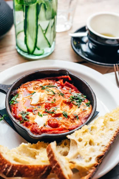 Baharatlı domates, kırmızı biber, feta, yumurta, kişniş ve ev yapımı ekşi hamur ile taze yapılmış shakshuka, demir tavada servis edilir, sağlıklı vejetaryen kahvaltısı.