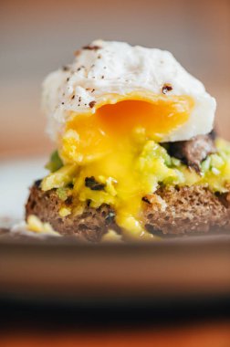 Haşlanmış yumurtadan sağlıklı bir kahvaltı, kırılmış avokado, ekşi ekmeğin üstünde ızgara mantar, yarısı yenmiş, seçici odaklanma, sığ DoF