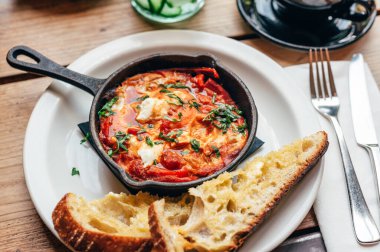 Baharatlı domates, kırmızı biber, feta, yumurta, kişniş ve ev yapımı ekşi hamur ile taze yapılmış shakshuka, demir tavada servis edilir, sağlıklı vejetaryen kahvaltısı.