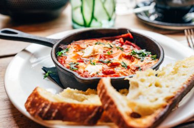 Baharatlı domates, kırmızı biber, feta, yumurta, kişniş ve ev yapımı ekşi hamur ile taze yapılmış shakshuka, demir tavada servis edilir, sağlıklı vejetaryen kahvaltısı.