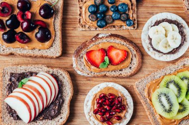 Various kind of open sandwiches with berries and fruits. Made from bread, such as wholegrain, rice crakers, crispbreads and different nut butter, such as peanut, crunchy cashew and almond butter