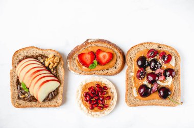 Various kind of open sandwiches with berries and fruits. Made from bread, such as wholegrain, rice crakers, crispbreads and different nut butter, such as peanut, crunchy cashew and almond butter