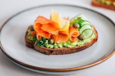 Toasted bread with mashed avocado, cucumber and smoked salmon on grey plate