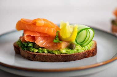 Toasted bread with mashed avocado, cucumber and smoked salmon on grey plate