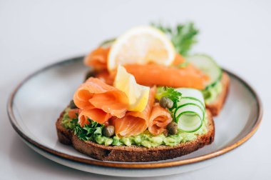 Toasted bread with mashed avocado, cucumber and smoked salmon on grey plate
