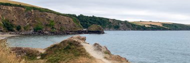 Rocky coastline near Par Beach and Polkerris Beach during cloudy rainy day, Gribbin Head, Cornwall, UK. Footpath along coast