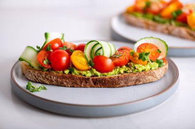 Tasty open sandwich from toasted sourdough bread with mashed avocado, slices of fresh cucumber and cherry tomatoes