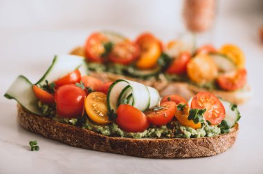 Tasty open sandwich from toasted sourdough bread with mashed avocado, slices of fresh cucumber and cherry tomatoes