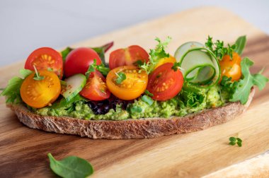 Tasty open sandwich from toasted sourdough bread with mashed avocado, slices of fresh cucumber and cherry tomatoes