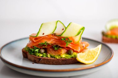 Toasted bread with mashed avocado, cucumber and smoked salmon on grey plate