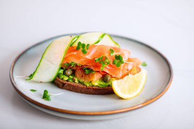 Toasted bread with mashed avocado, cucumber and smoked salmon on grey plate
