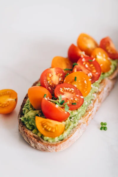 Tasty open sandwich from toasted sourdough bread with mashed avocado and fresh tomatoes